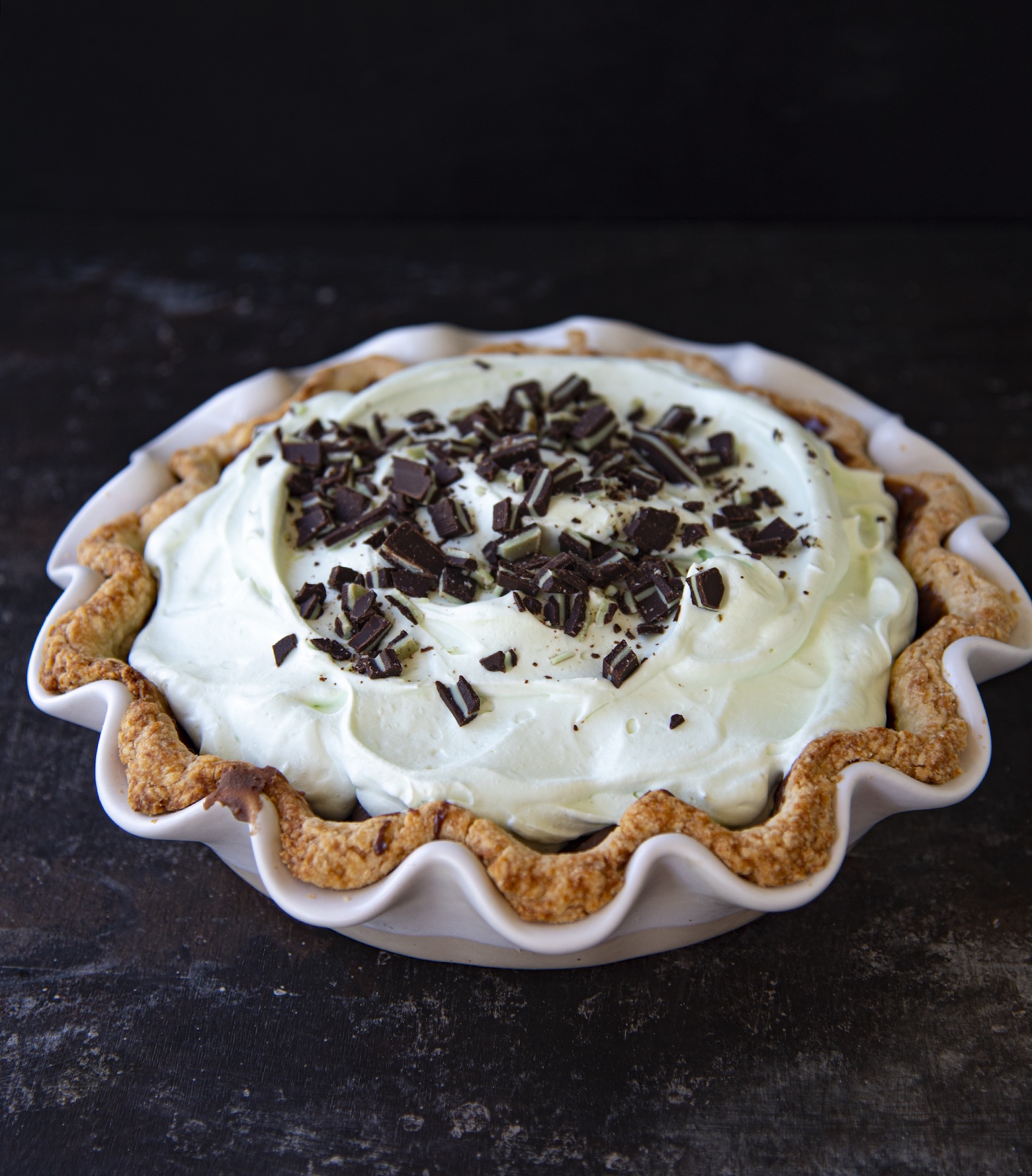 Shot of the whole pie. The pie has green whipped cream and has pieces of Andes Mints on top.